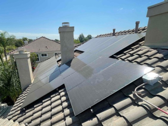 Three rows of solar panels surround a chimney on a residential roof.