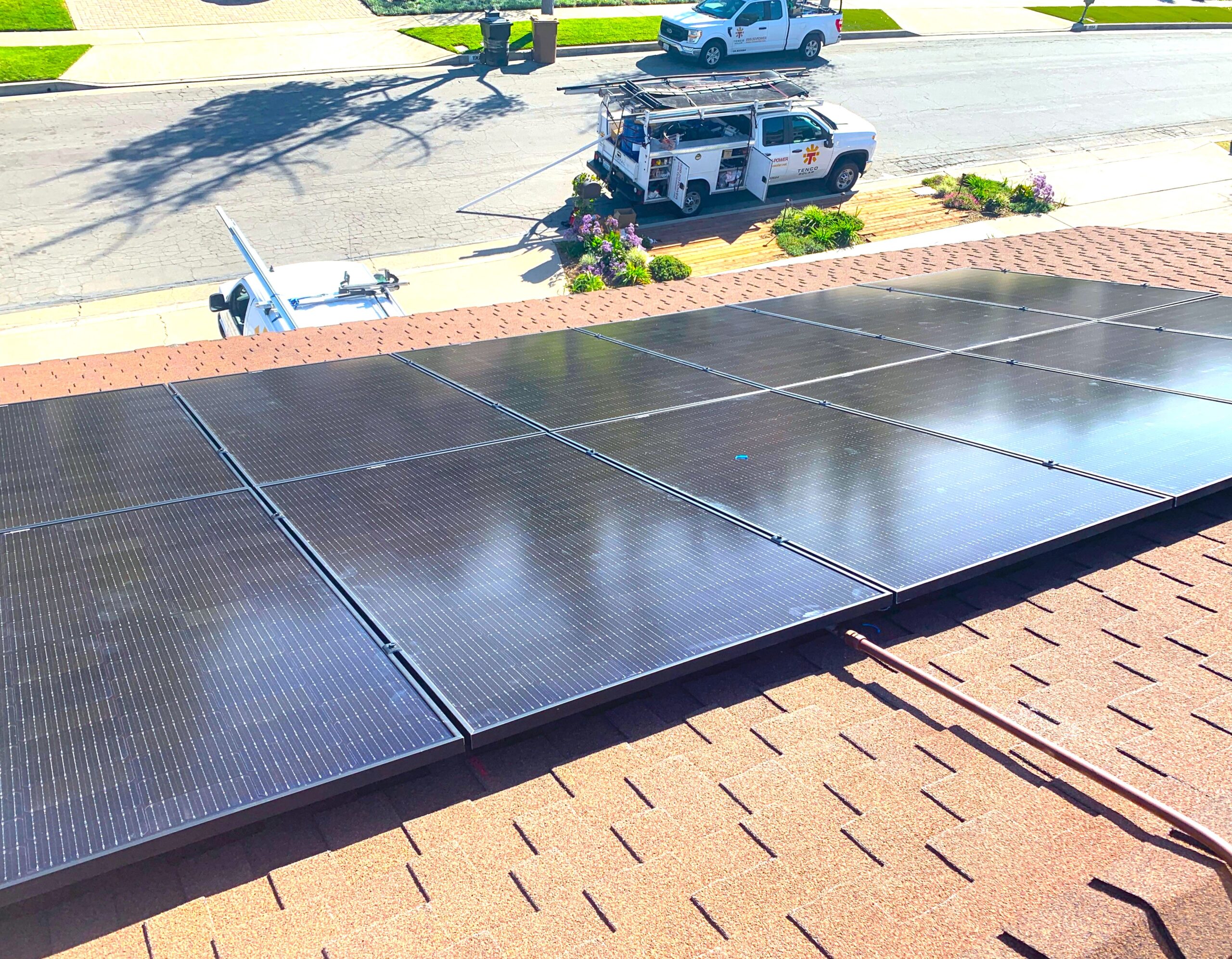 A close shot of solar panels on the roof of a house with a TENCO SOLAR service truck on the street below