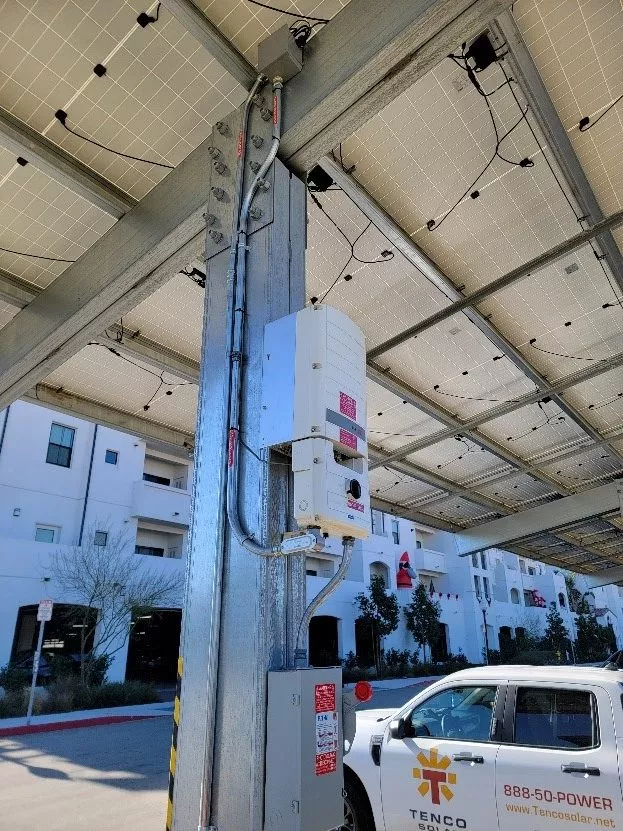 The underside of solar panels covering a carport and the battery they are connected to